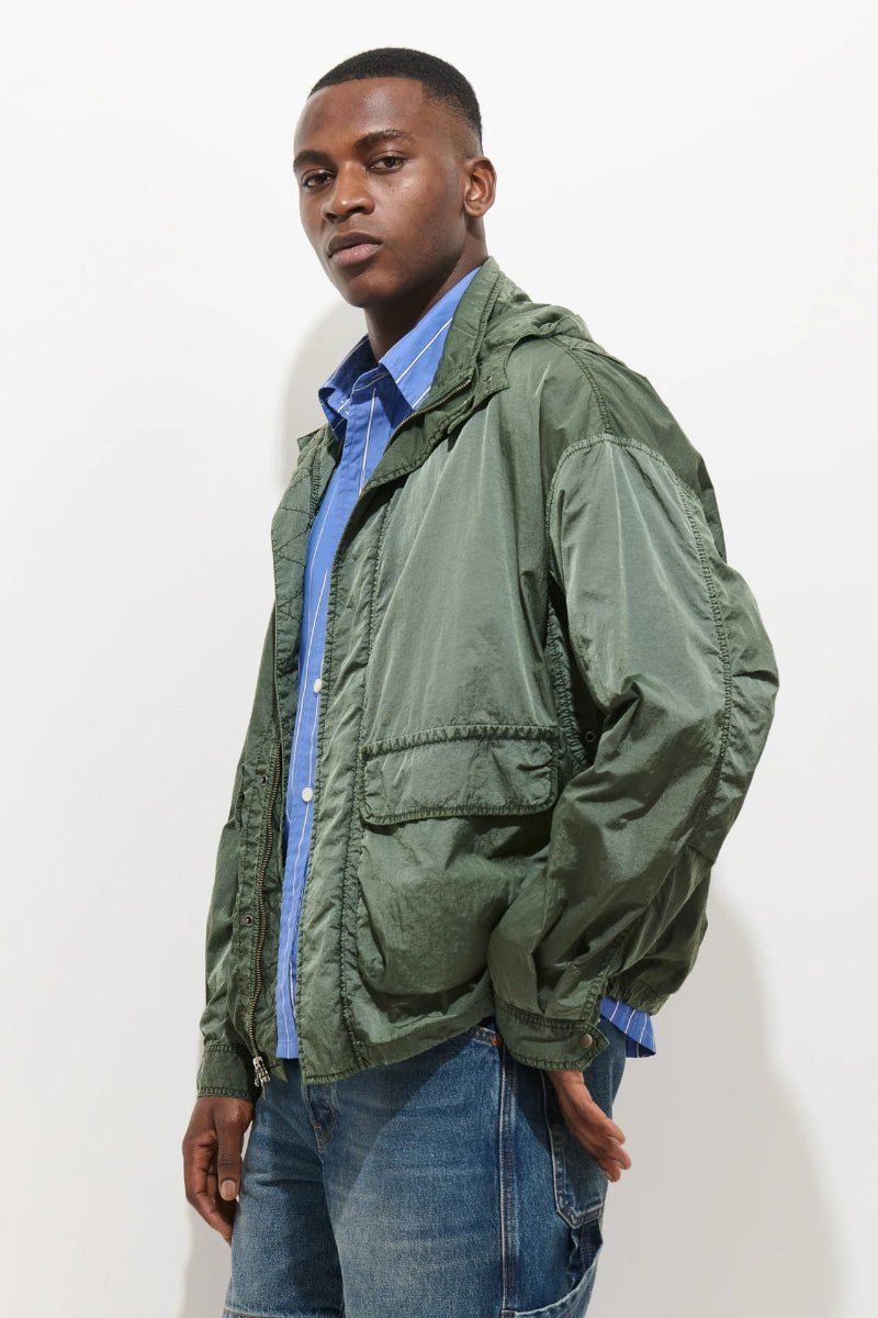 Man wearing a green jacket over a blue shirt and jeans on a white background