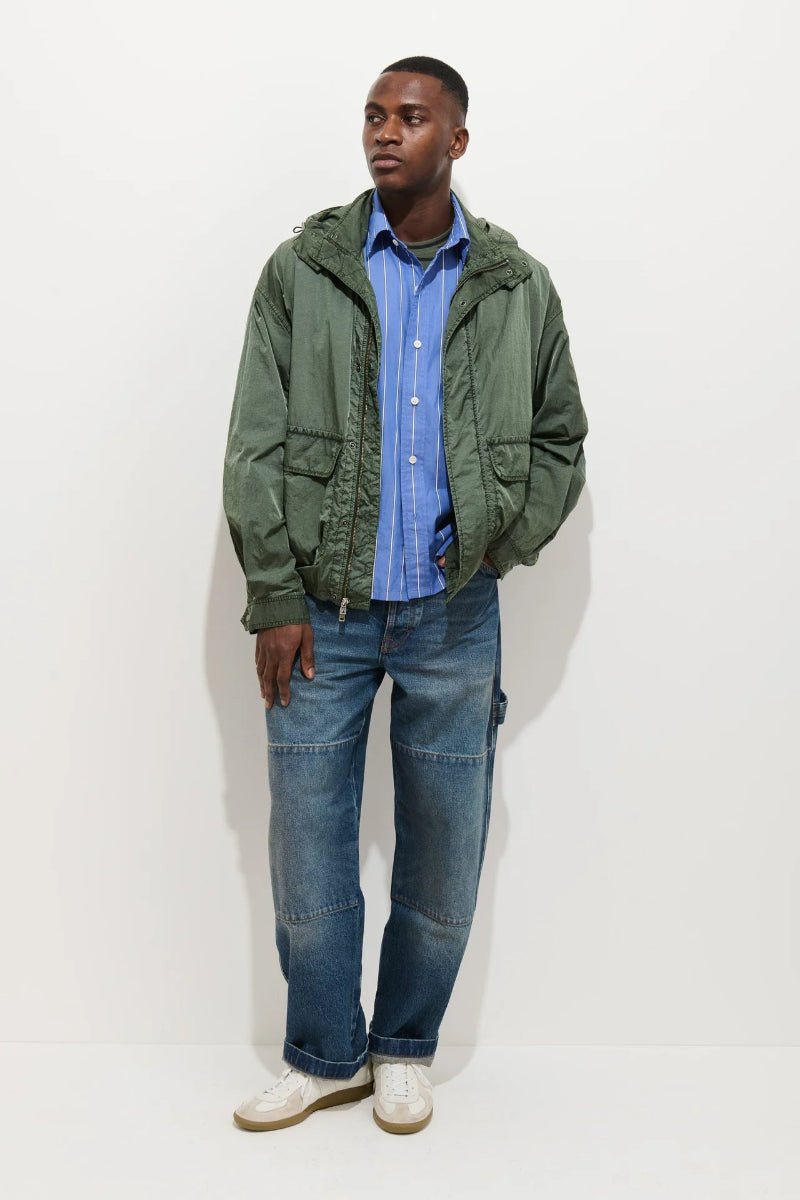 Man wearing a green jacket, blue shirt, and jeans on a white background
