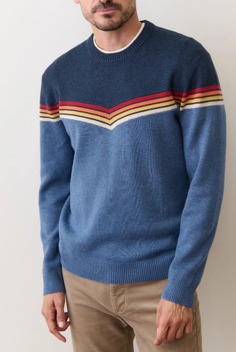 Man wearing a blue sweater with colorful stripes on a plain background