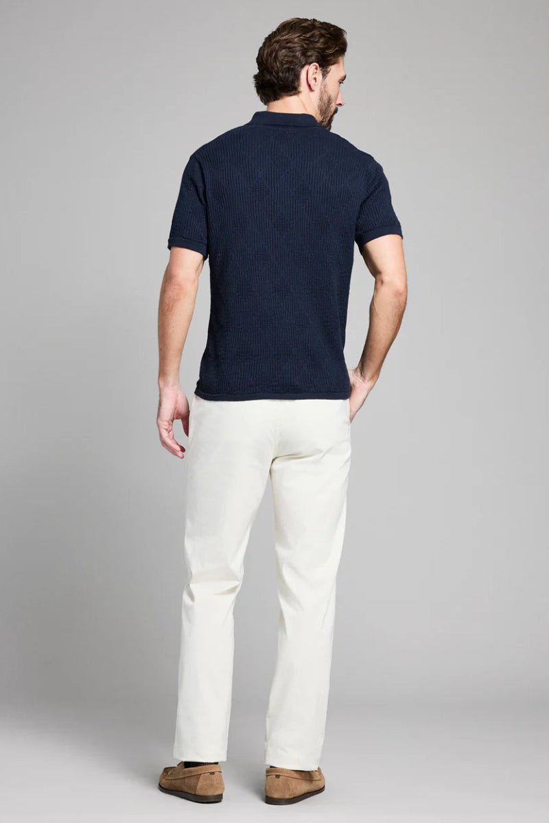 Man wearing a navy polo shirt and white pants on a gray background