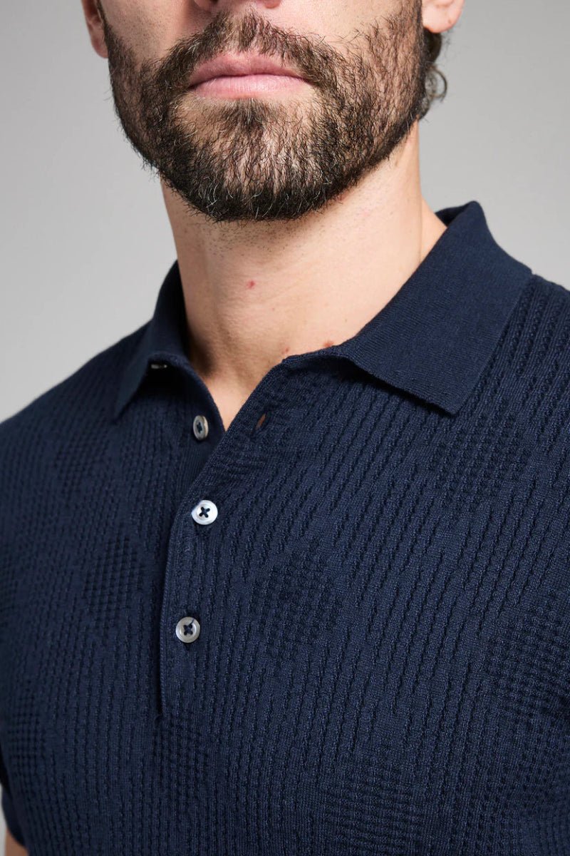 Man wearing a navy blue textured polo shirt against a gray background