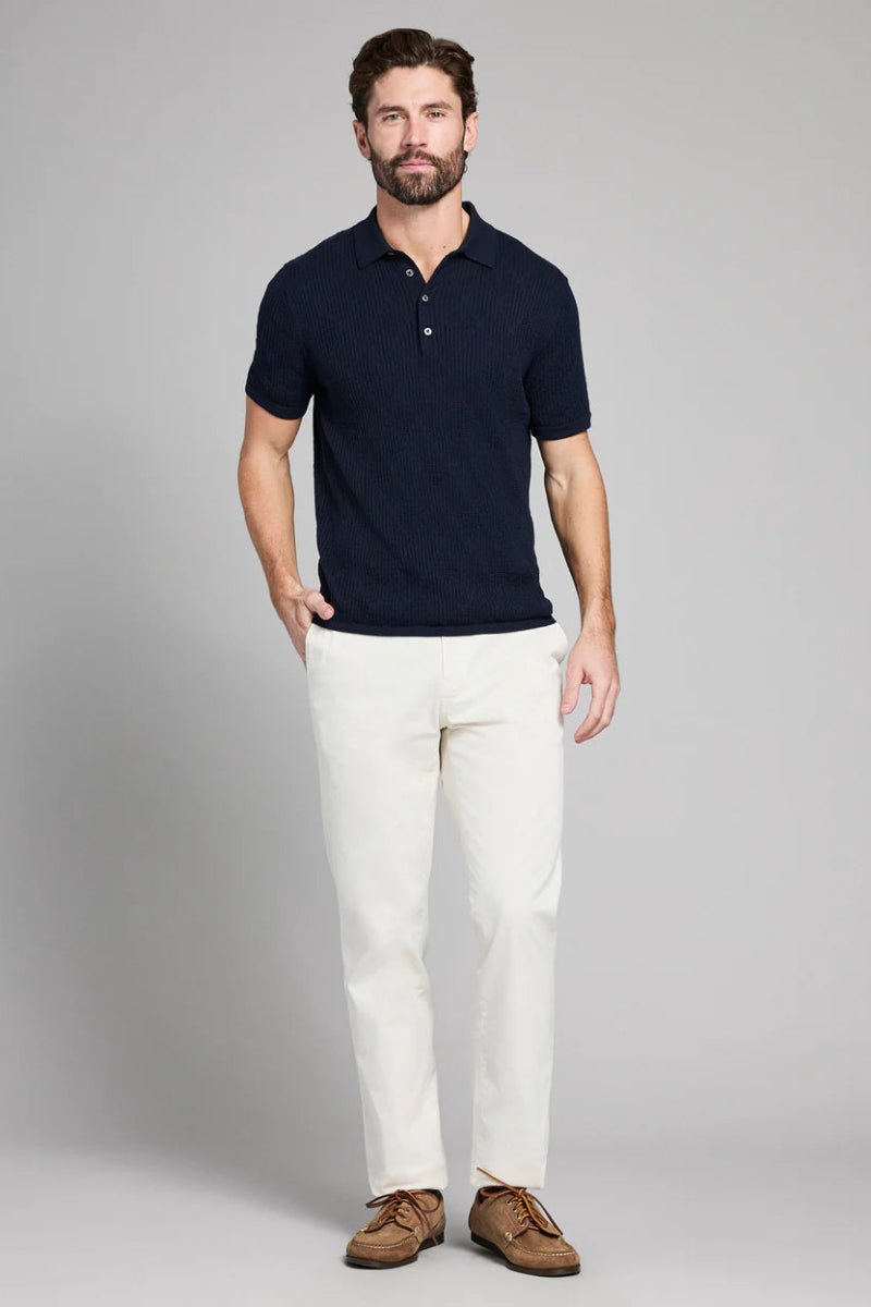Man wearing a navy polo shirt and white pants on a gray background
