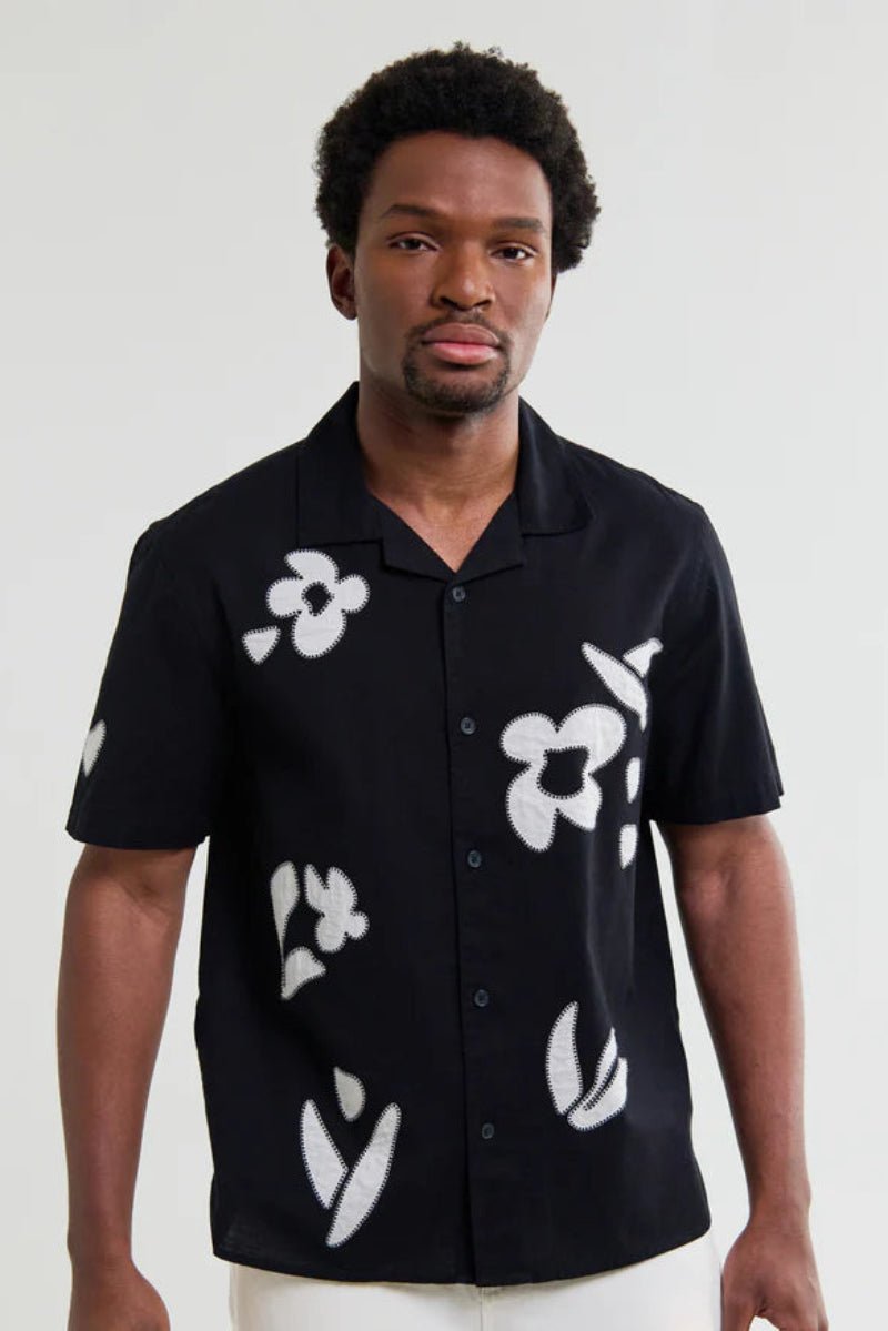 Man wearing a black shirt with white floral patterns against a plain background