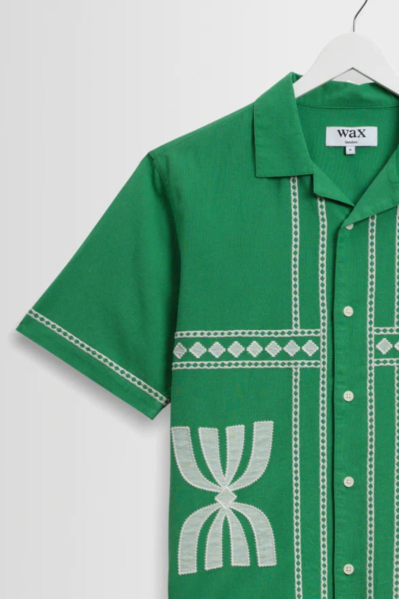 Green shirt with white patterns on a hanger against a white background