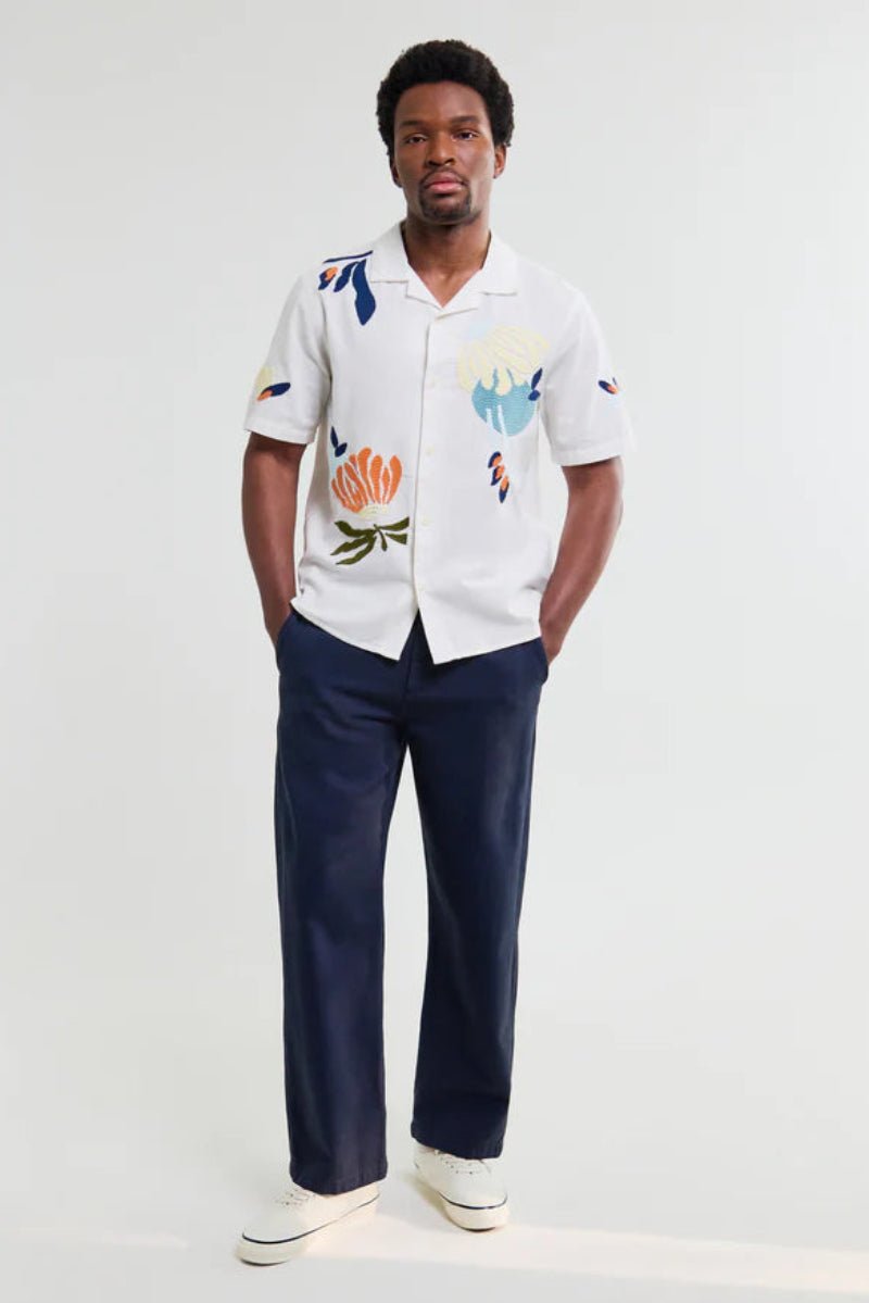 Man wearing a white shirt with colorful patterns and navy pants on a white background