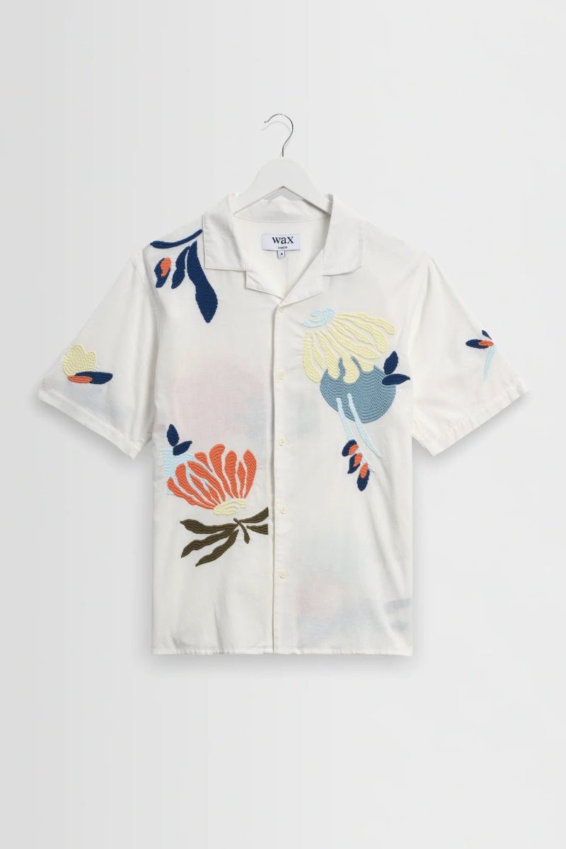 White shirt with colorful floral and butterfly designs on a hanger against a white background