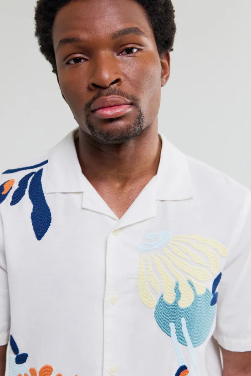 Man wearing a white shirt with colorful floral patterns on a plain background