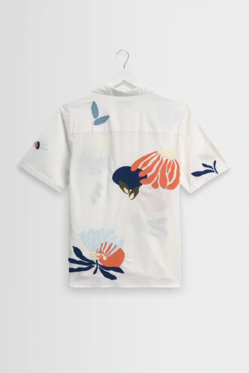 White shirt with colorful floral patterns on a hanger against a white background