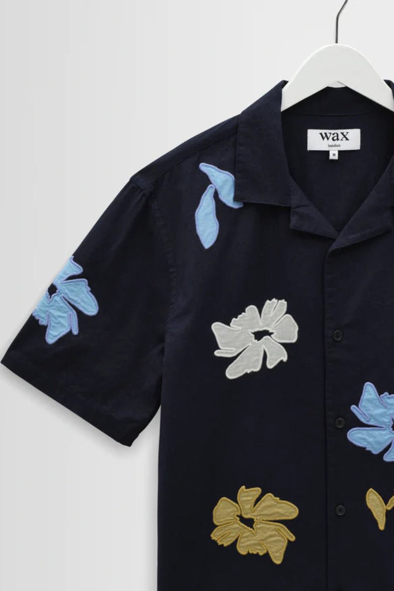 Black shirt with floral appliqués on a hanger against a white background