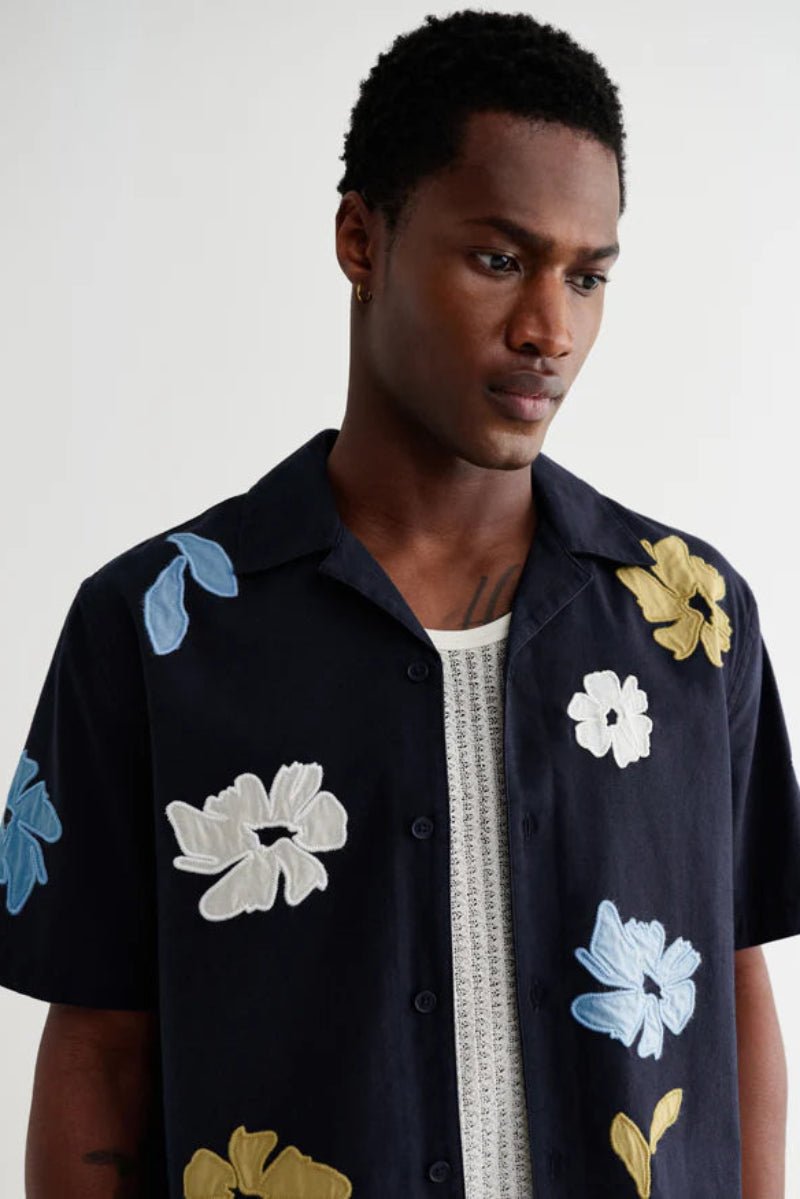 Man wearing a black shirt with floral patterns on a plain background
