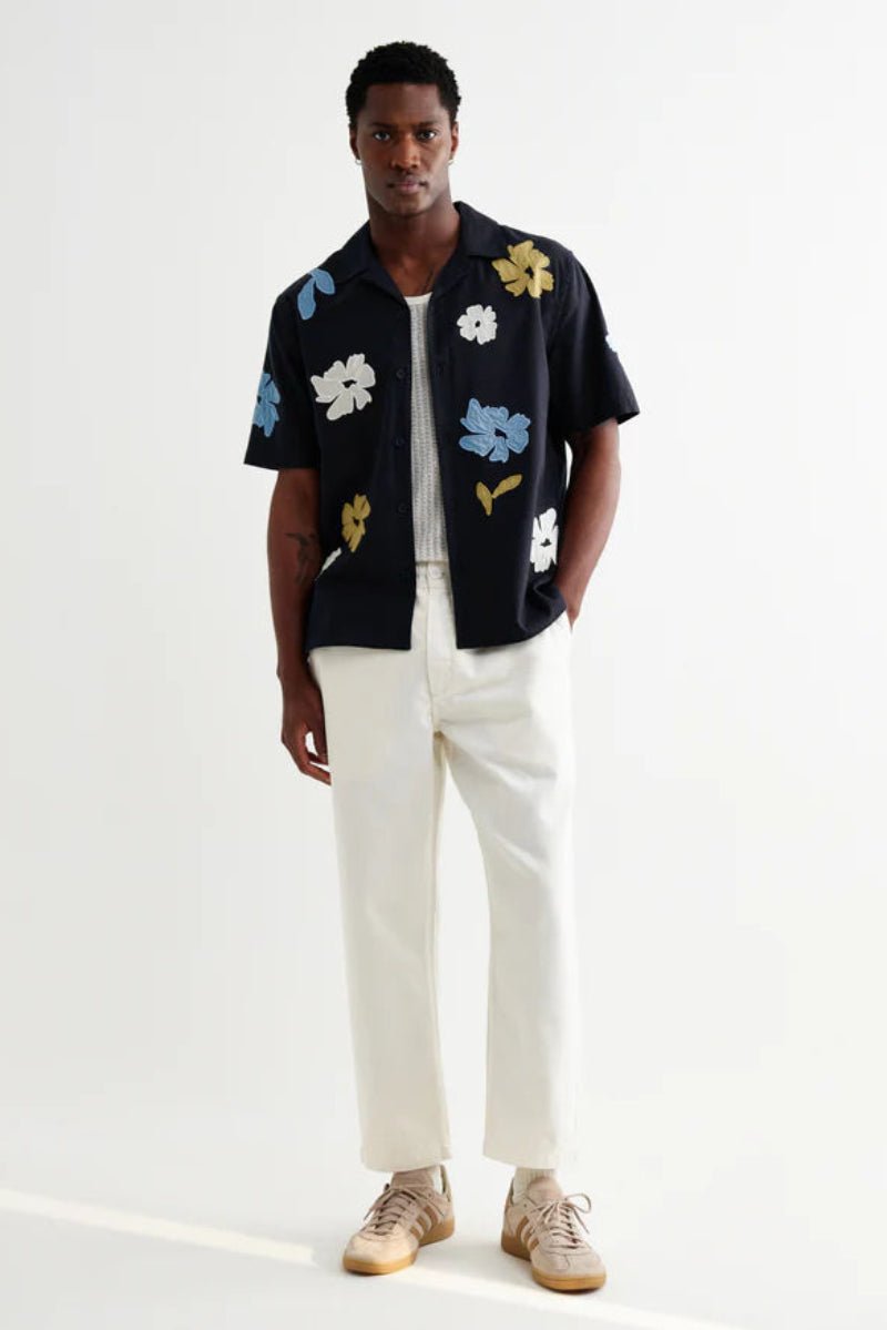 Man wearing a black floral shirt with white pants on a white background