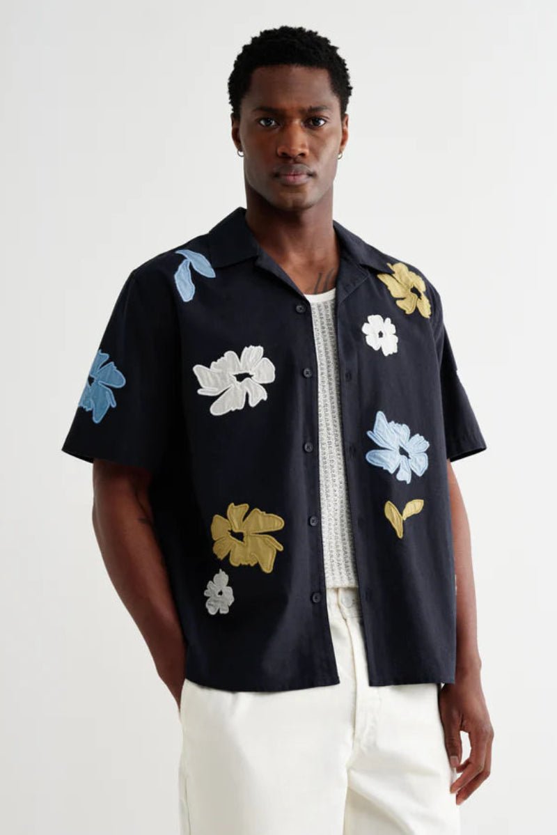 Man wearing a black short-sleeve shirt with colorful floral patterns on a white background