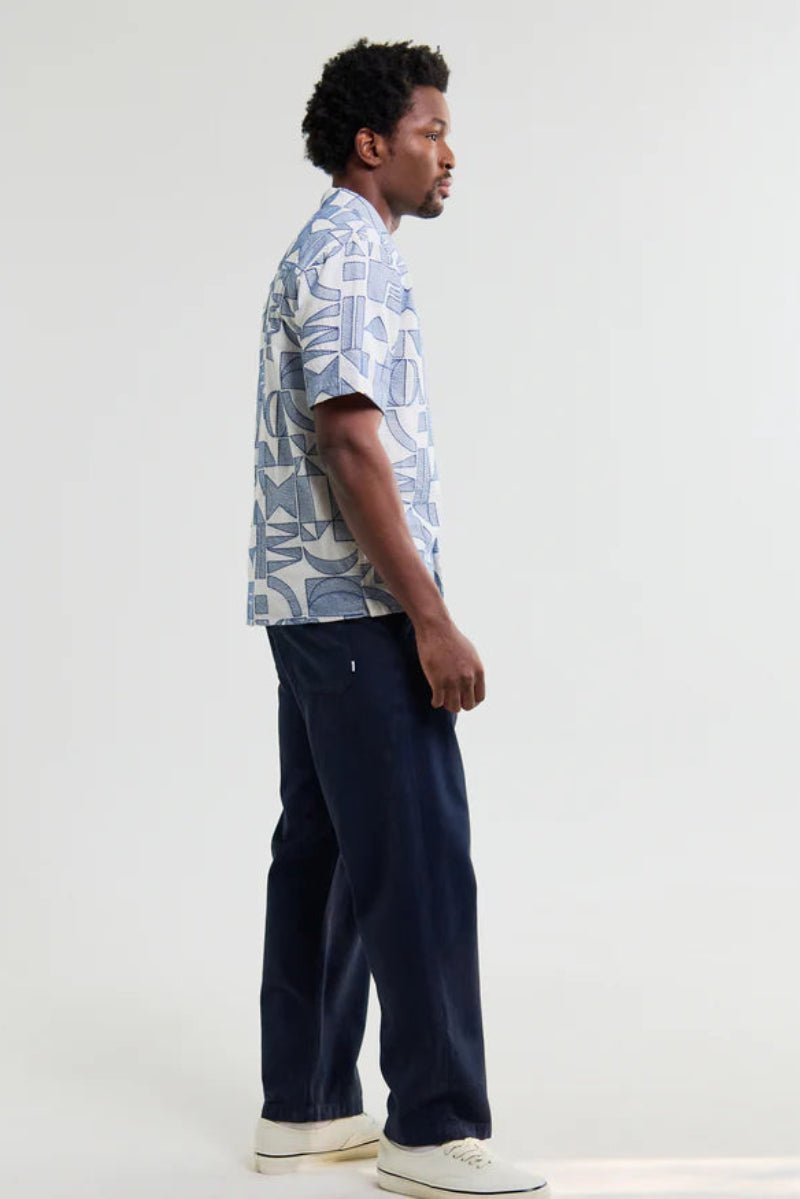 Man wearing a patterned shirt and dark pants on a white background