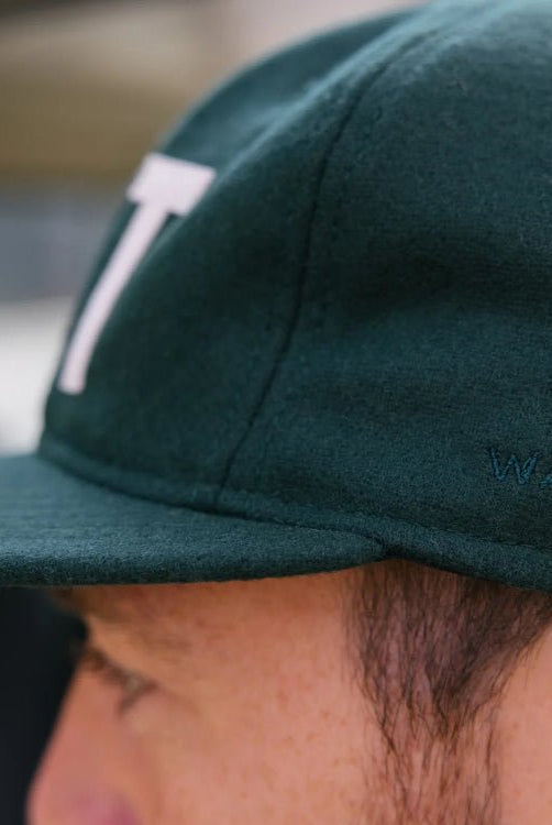 Close-up of a person wearing a green cap with a logo, blurred background