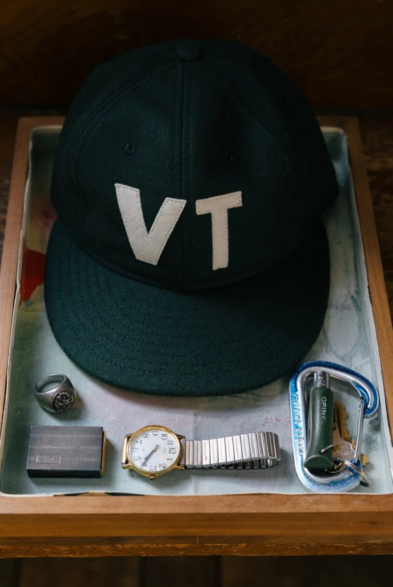 Green cap with 'VT' on a wooden tray with other items
