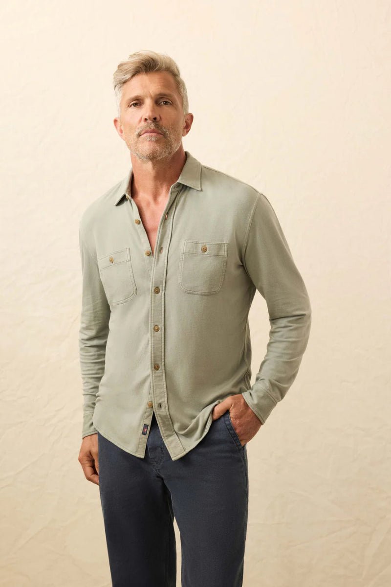 Man wearing a light green button-up shirt and dark pants against a beige background