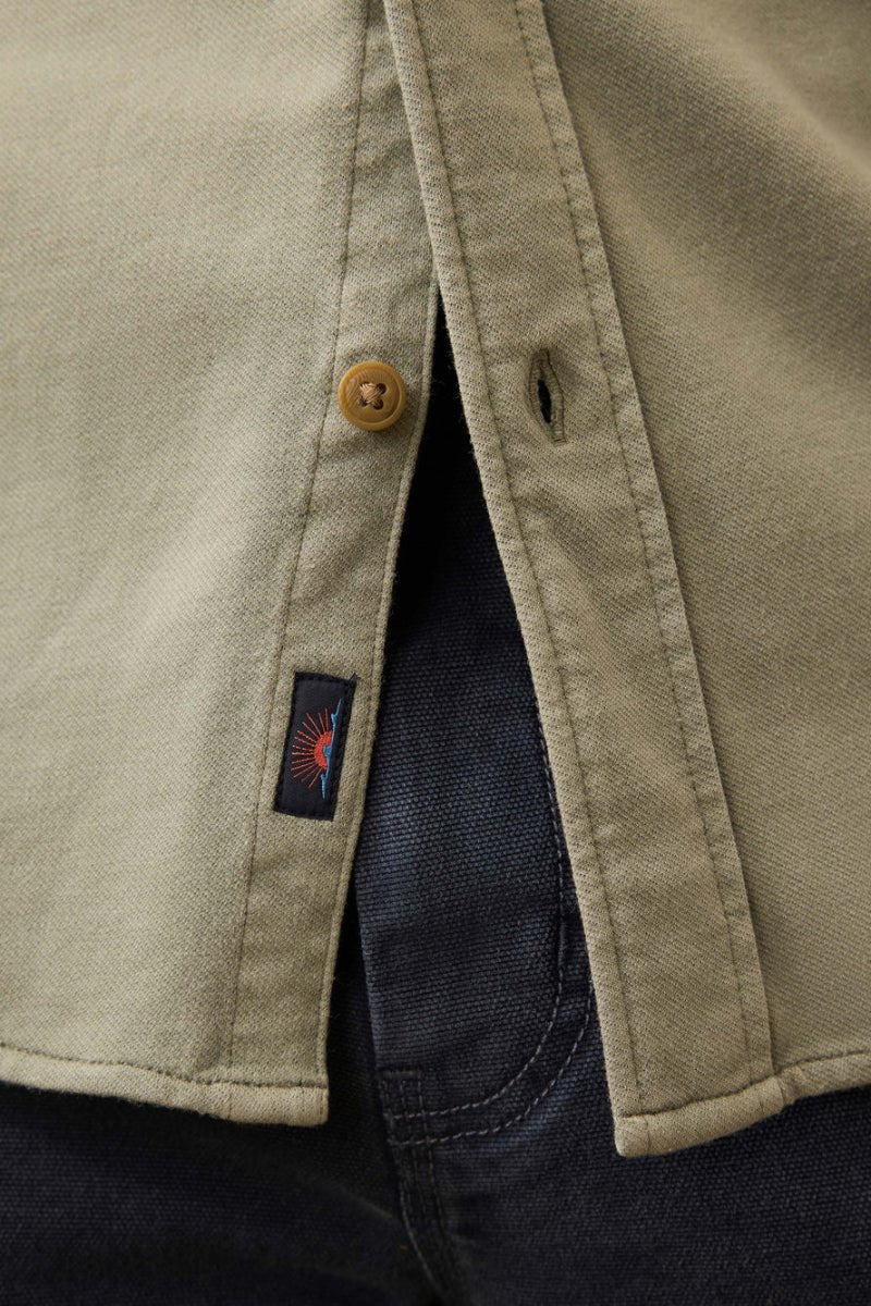 Close-up of a beige jacket with a button and a brand logo on a dark background