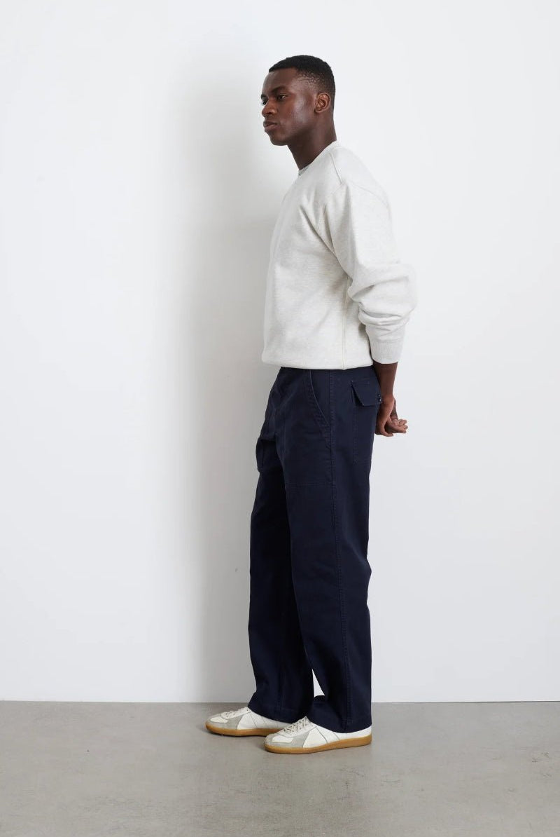 Man wearing a white sweater and navy pants standing against a plain white wall.