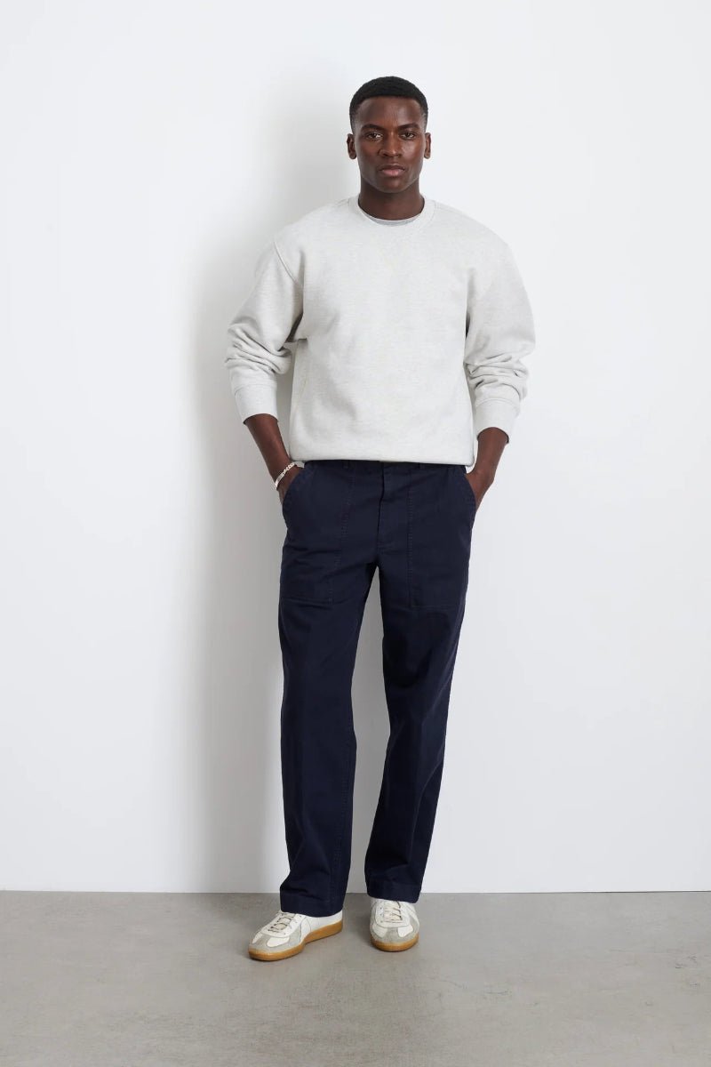 Man wearing a white sweater and navy pants against a plain background