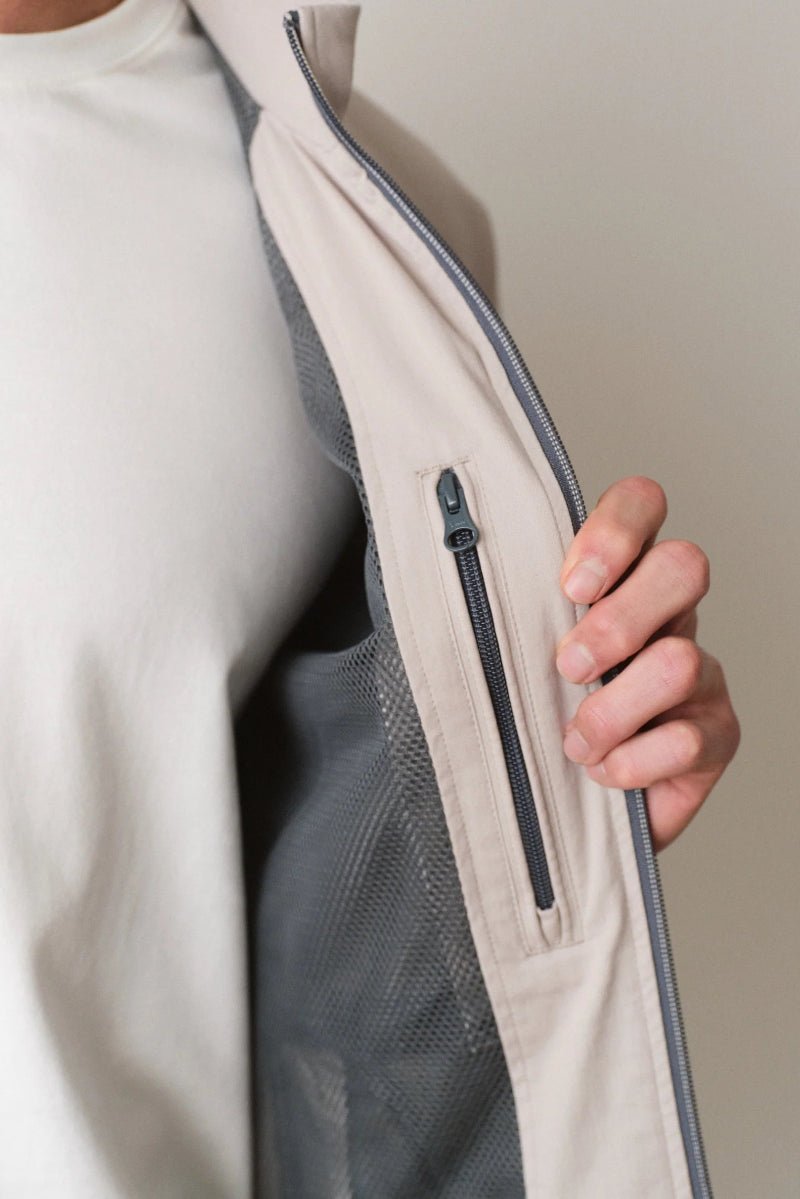 Close-up of a person wearing a light-colored jacket with a zipper pocket.