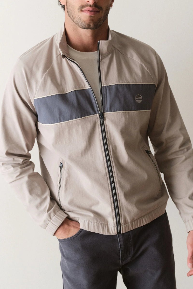 Man wearing a beige jacket with a blue stripe on a plain background