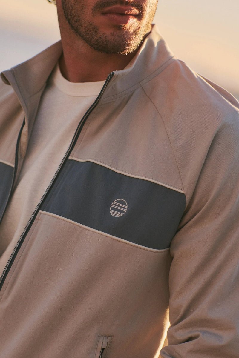 Man wearing a beige jacket with a logo on a blurred background
