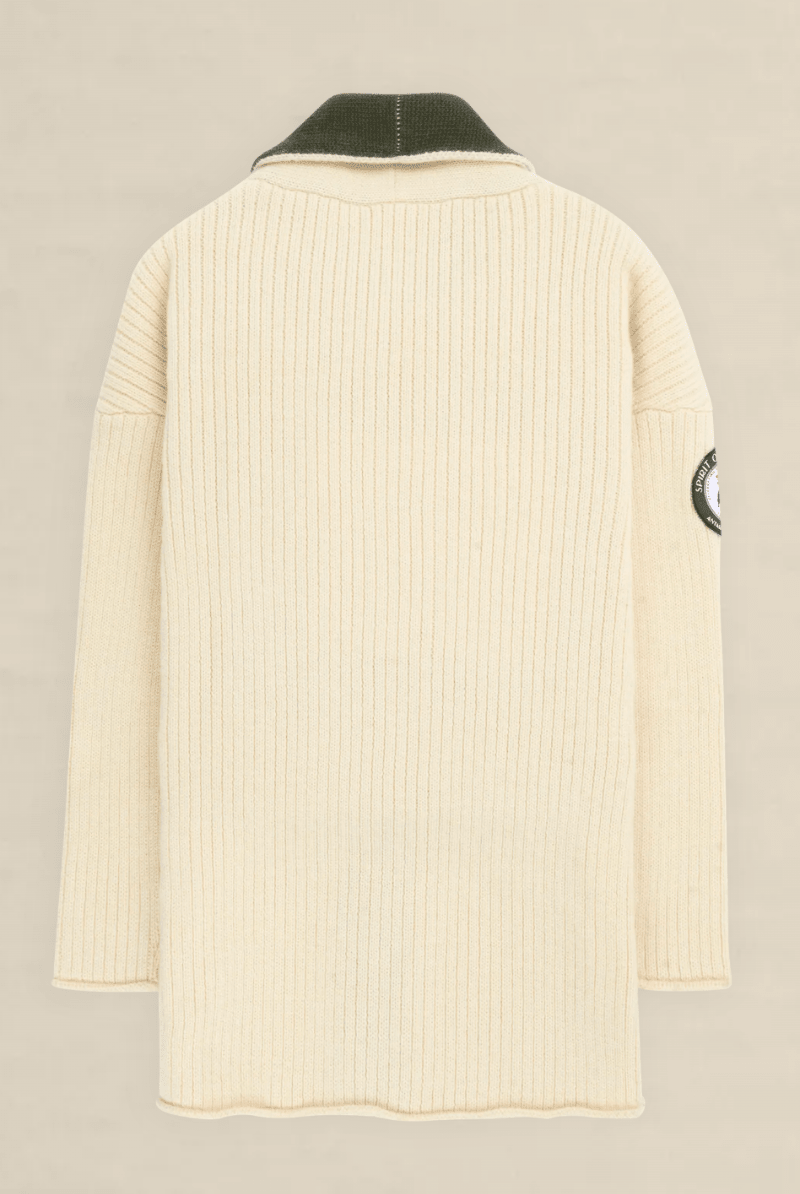 A cream-colored ribbed knit sweater shown from the back, featuring a dark olive green collar and a circular patch on the left sleeve, set against a light beige background.