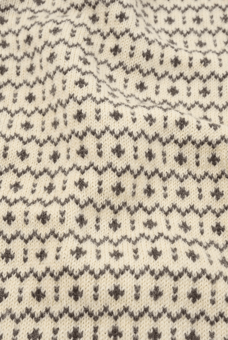 Close-up of a cream-colored knit fabric with a dark gray Fair Isle pattern of small geometric motifs.