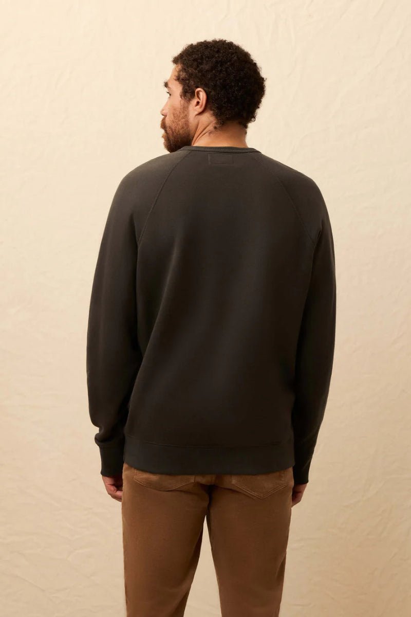 Man wearing a black sweater and brown pants against a beige background