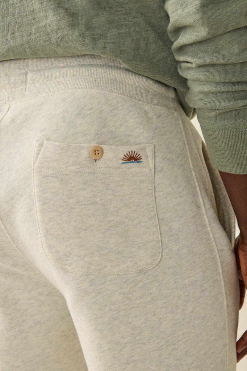 Light gray sweatpants with embroidered designs on the pocket, worn by a person.