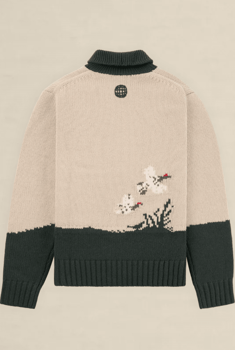Back view of a knit sweater in beige and dark green, featuring a small embroidered floral motif near the lower right side and a circular black logo patch at the neck.