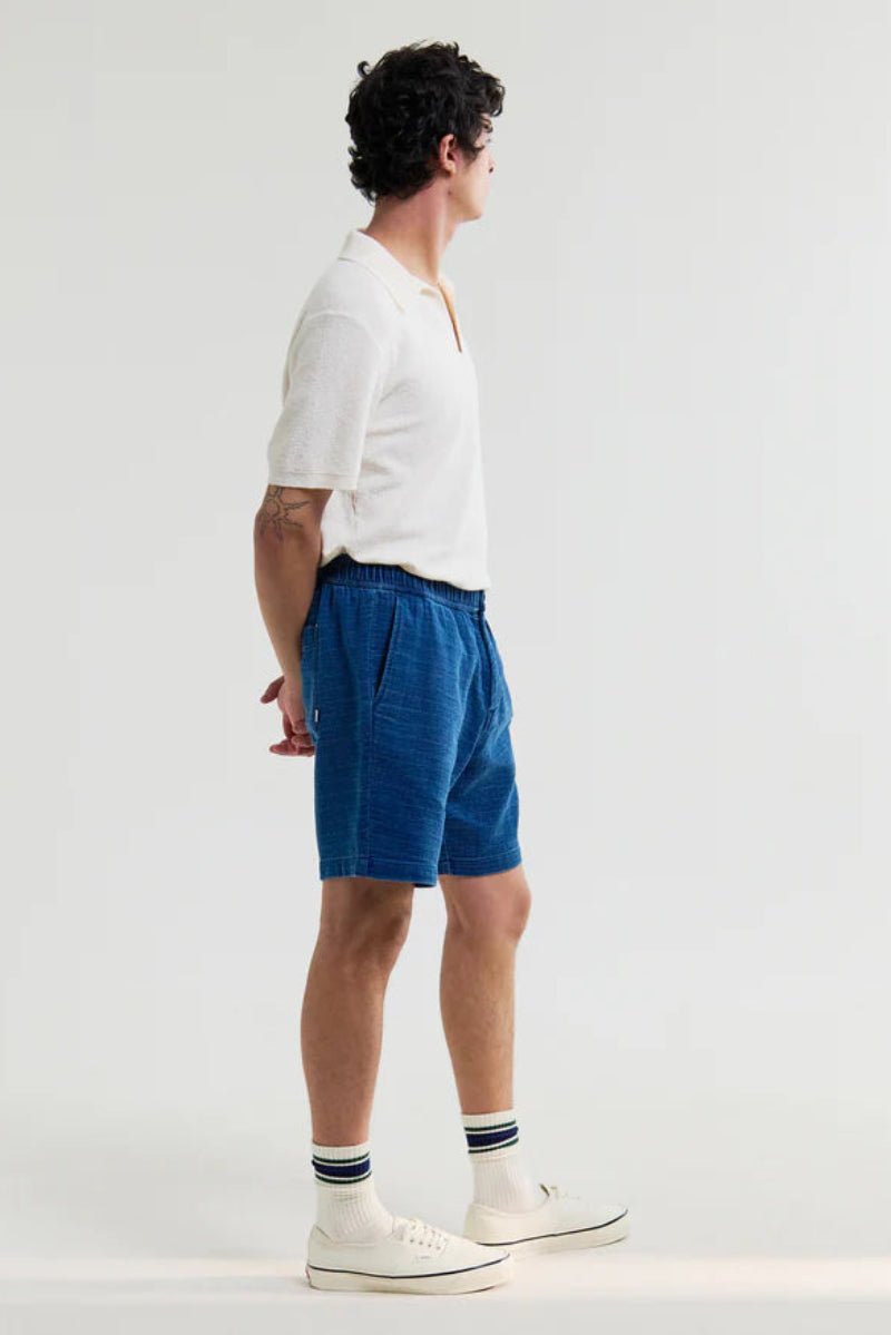 Person wearing a white shirt and blue shorts on a plain background