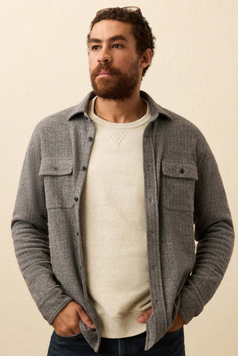 Man wearing a gray button-up shirt over a white sweater against a beige background