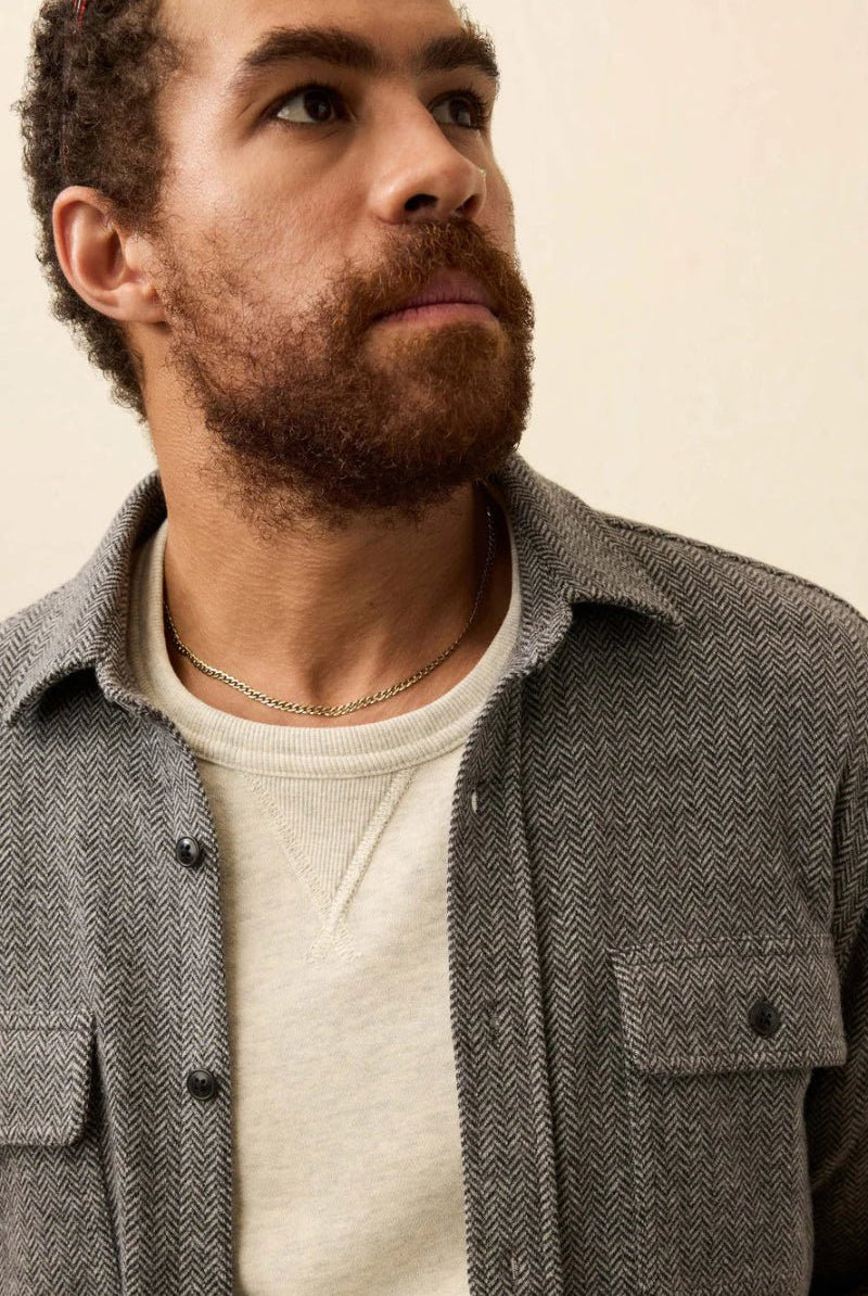 Man wearing a gray textured shirt over a white sweater against a beige background