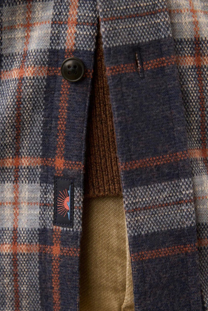 Close-up of a plaid jacket with a button and a visible brand logo.