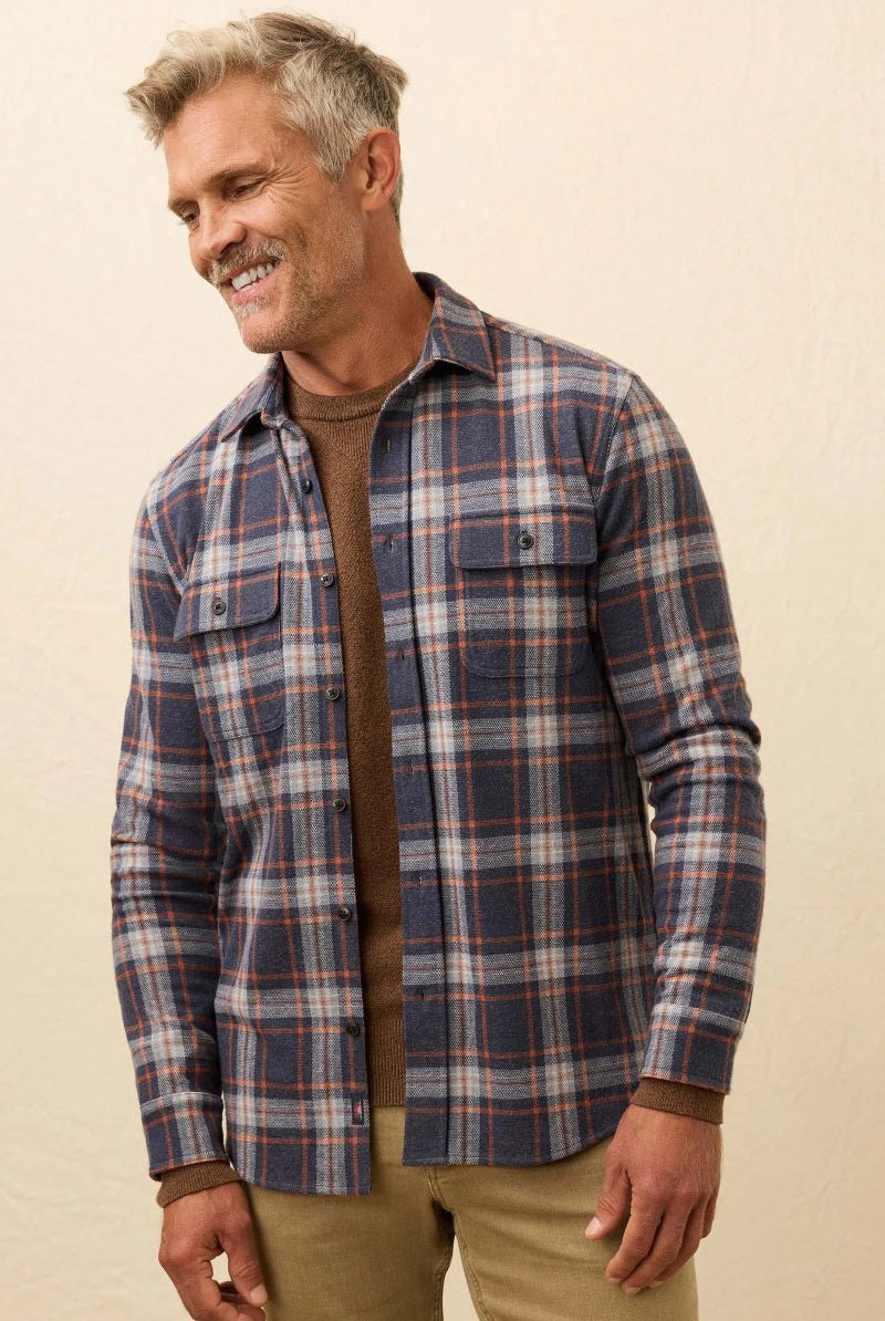Man wearing a plaid shirt over a brown sweater on a beige background