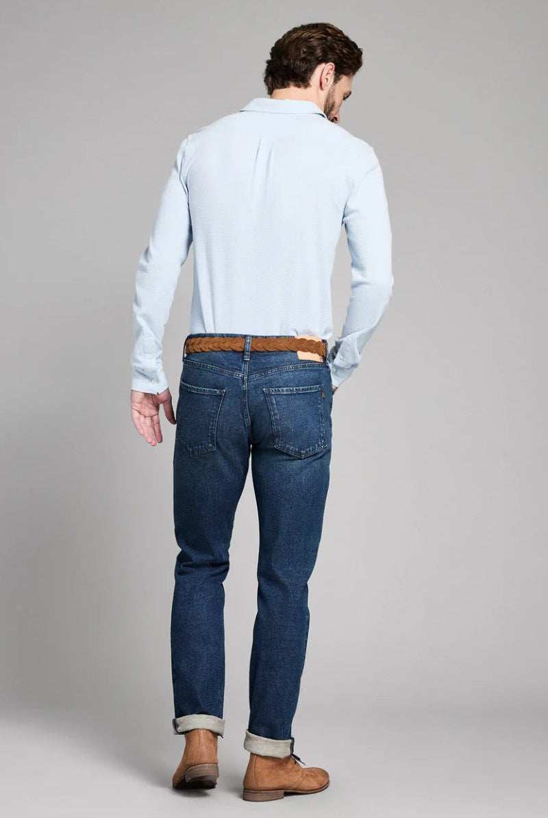 Man wearing a light blue shirt and dark blue jeans on a gray background