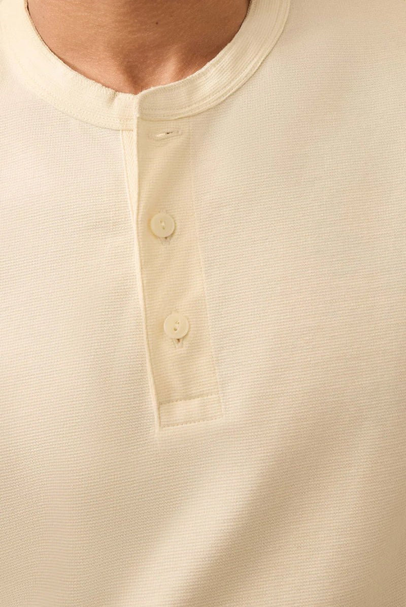 Close-up of a beige henley shirt with buttons on a plain background