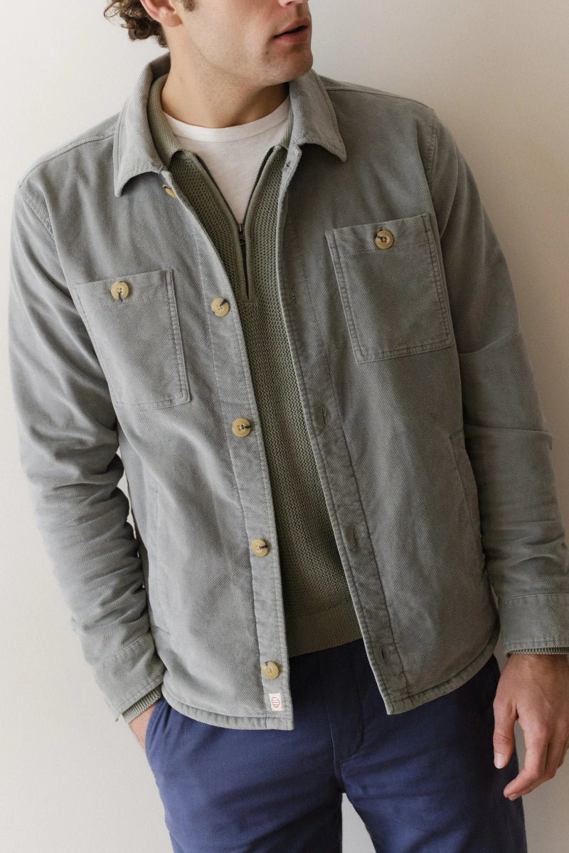 Man wearing a light gray jacket with gold buttons against a plain background