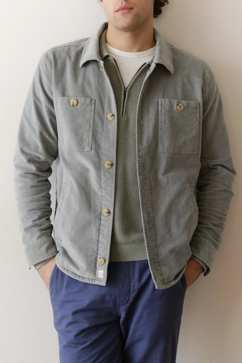 Person wearing a light gray jacket with button details against a plain background