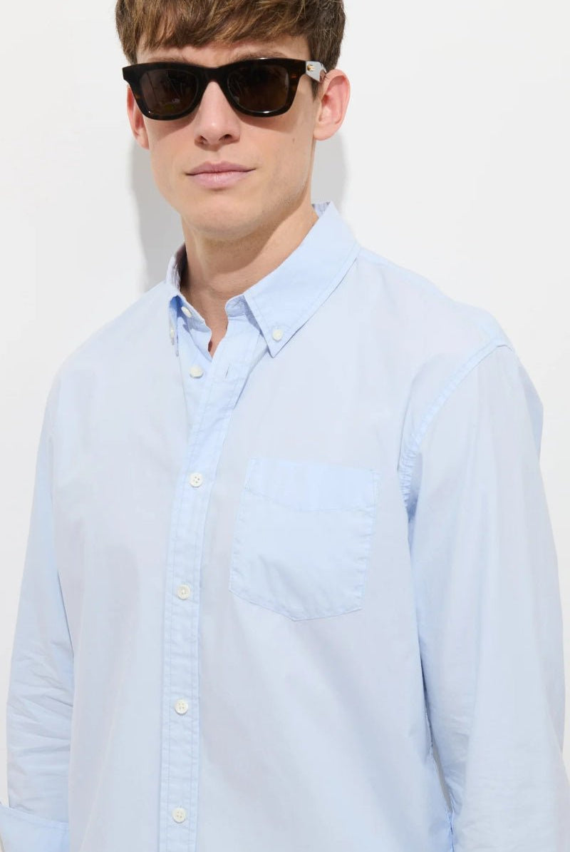 Man wearing a light blue button-up shirt and sunglasses against a white background