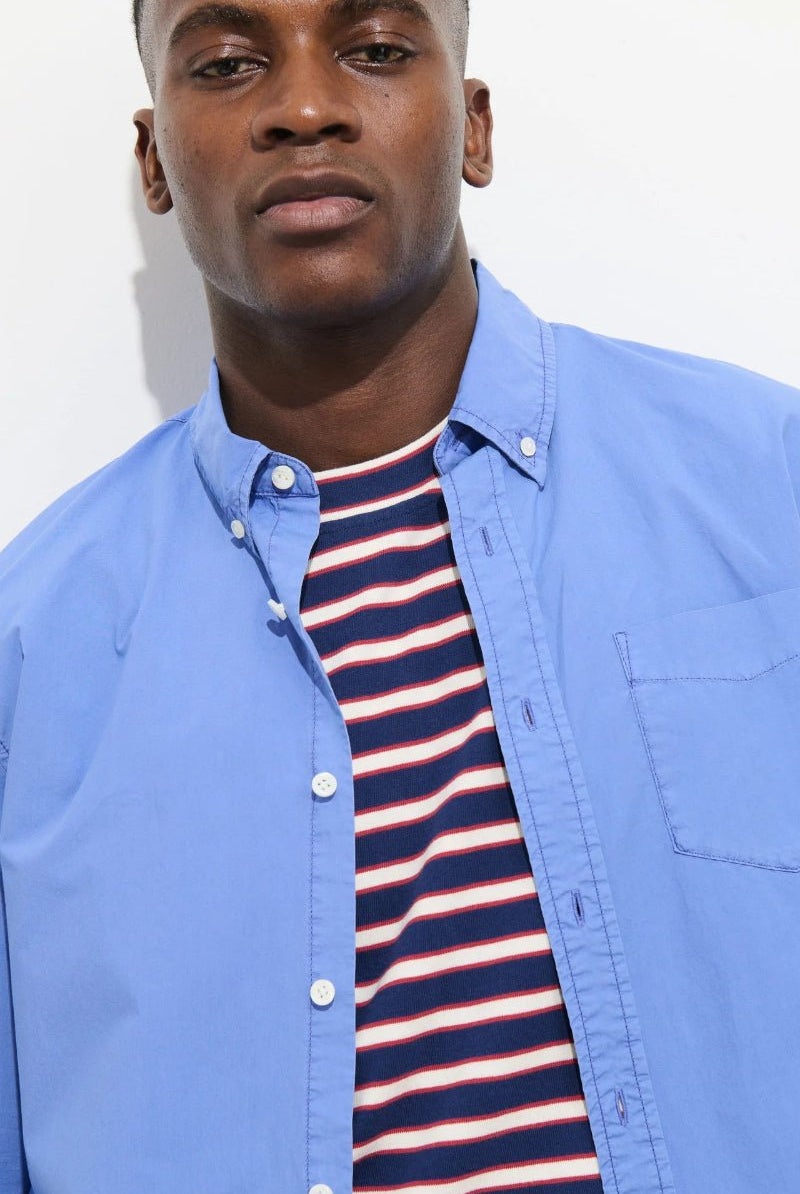 Man wearing a blue shirt over a striped shirt against a white background