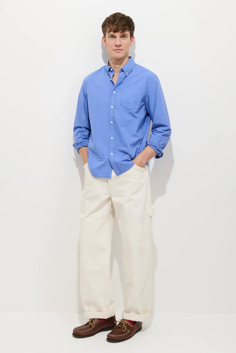 Man wearing a blue shirt and white pants on a light gray background