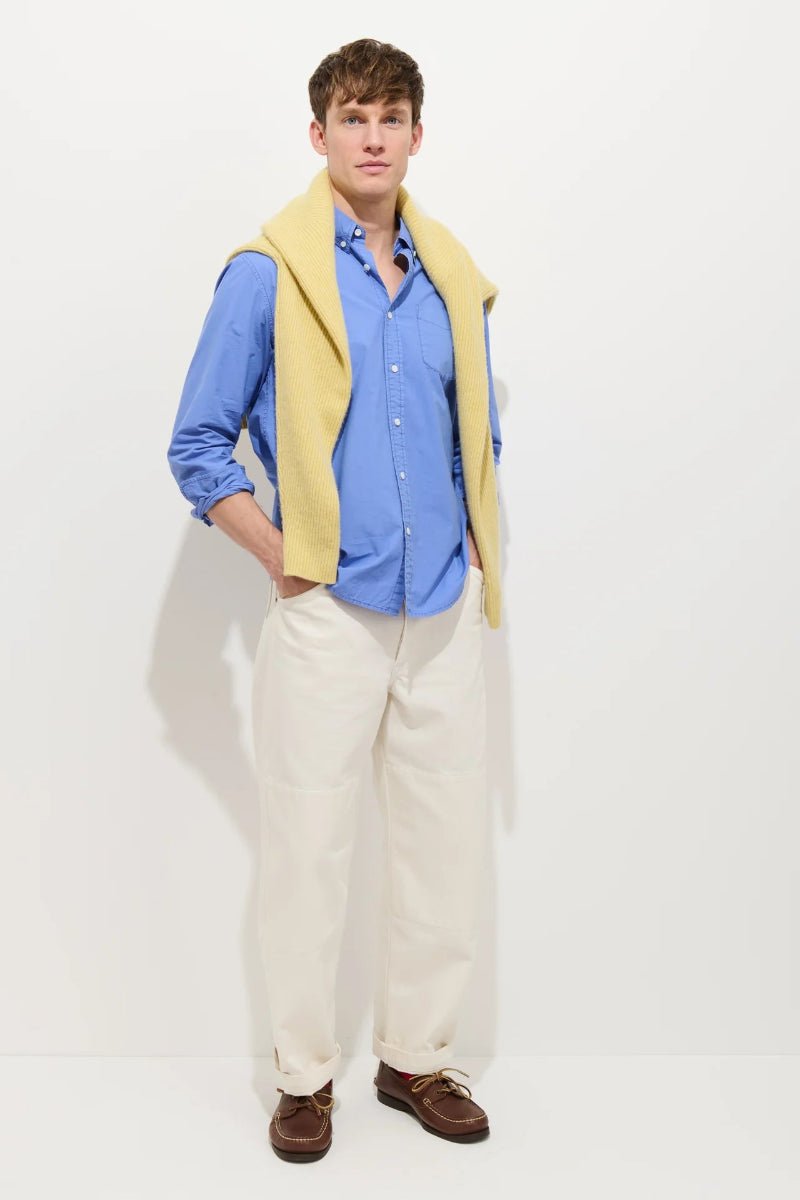 Man wearing a blue shirt, yellow vest, white pants, and brown shoes on a white background