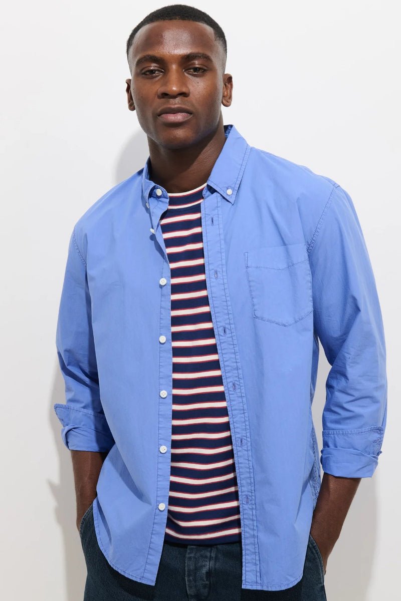 Man wearing a blue shirt over a striped shirt against a plain background