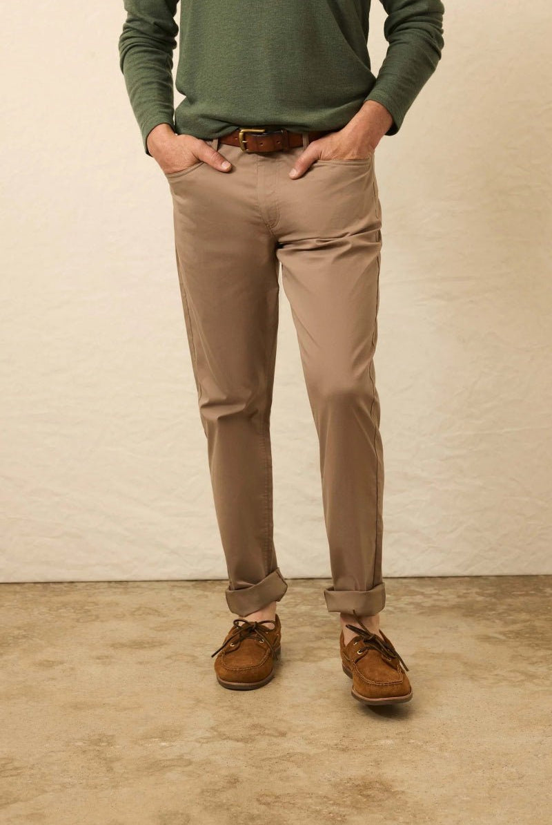 Person wearing a green sweater, beige pants, and brown shoes against a plain background