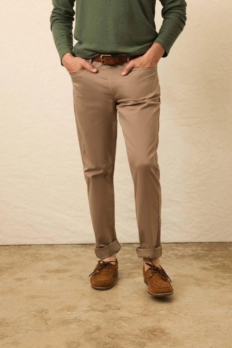 Person wearing a green sweater, beige pants, and brown shoes against a plain background