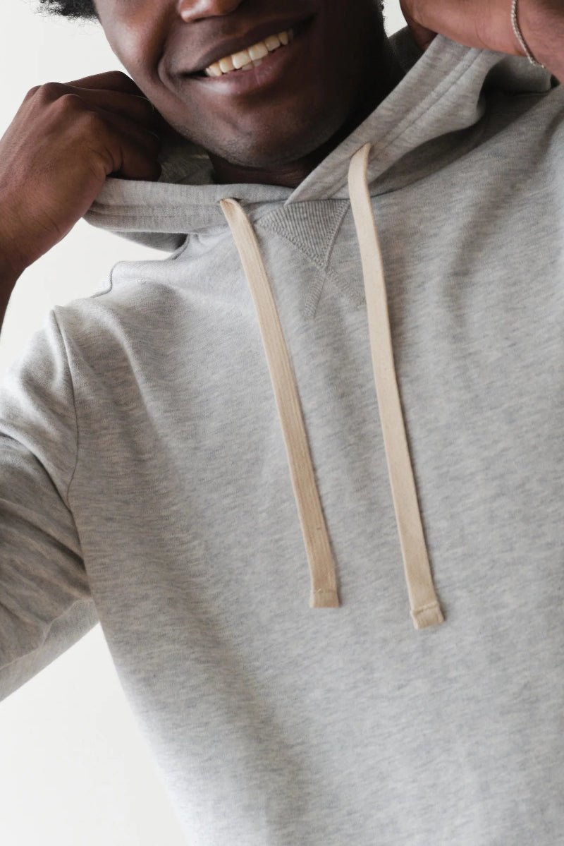 Person wearing a gray hoodie with beige drawstrings on a light background