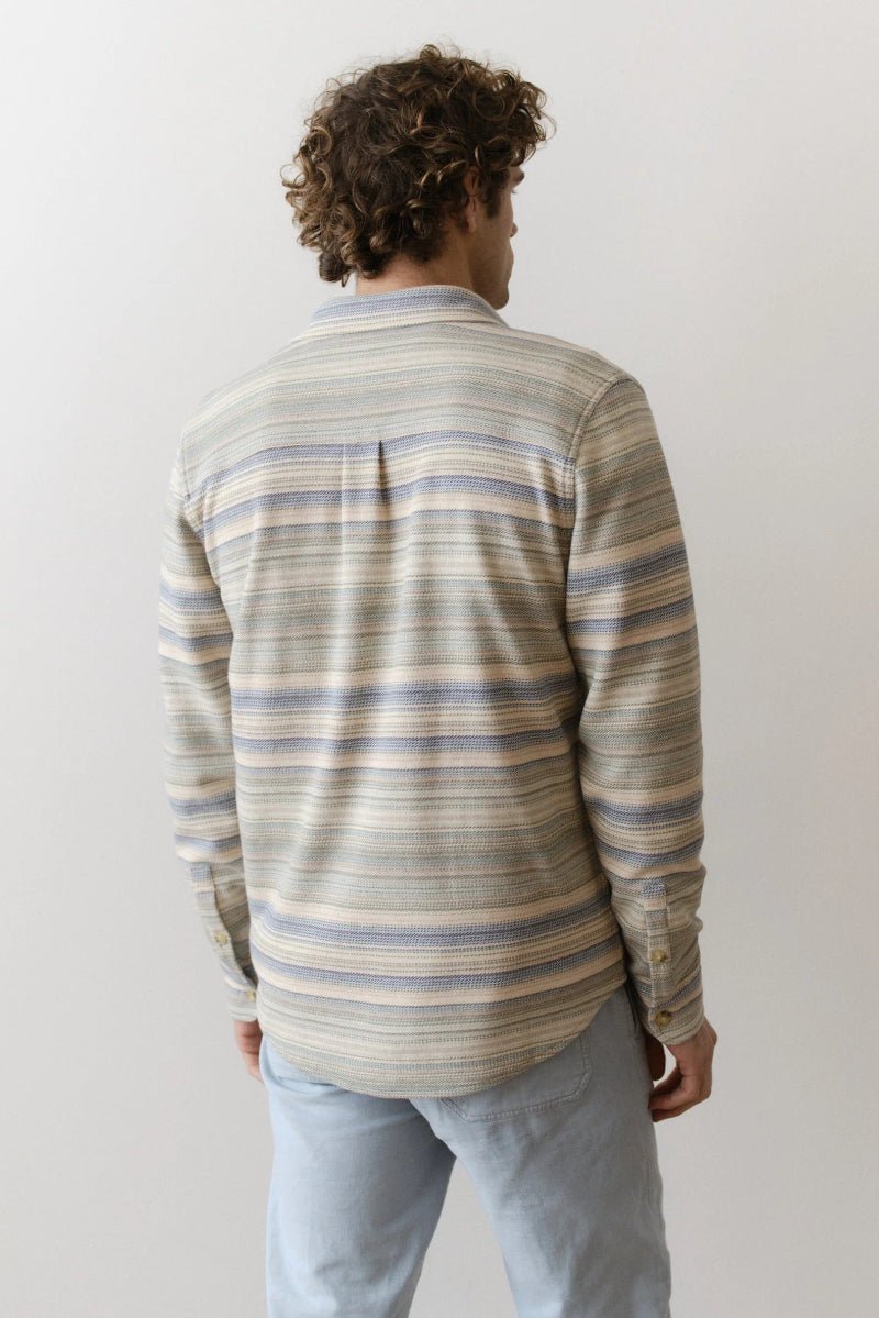 Person wearing a striped long-sleeve shirt and light blue jeans against a plain background