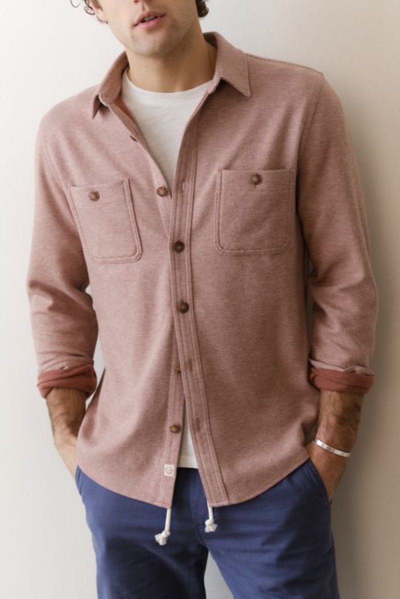 Person wearing a pink button-up shirt with rolled-up sleeves against a plain background